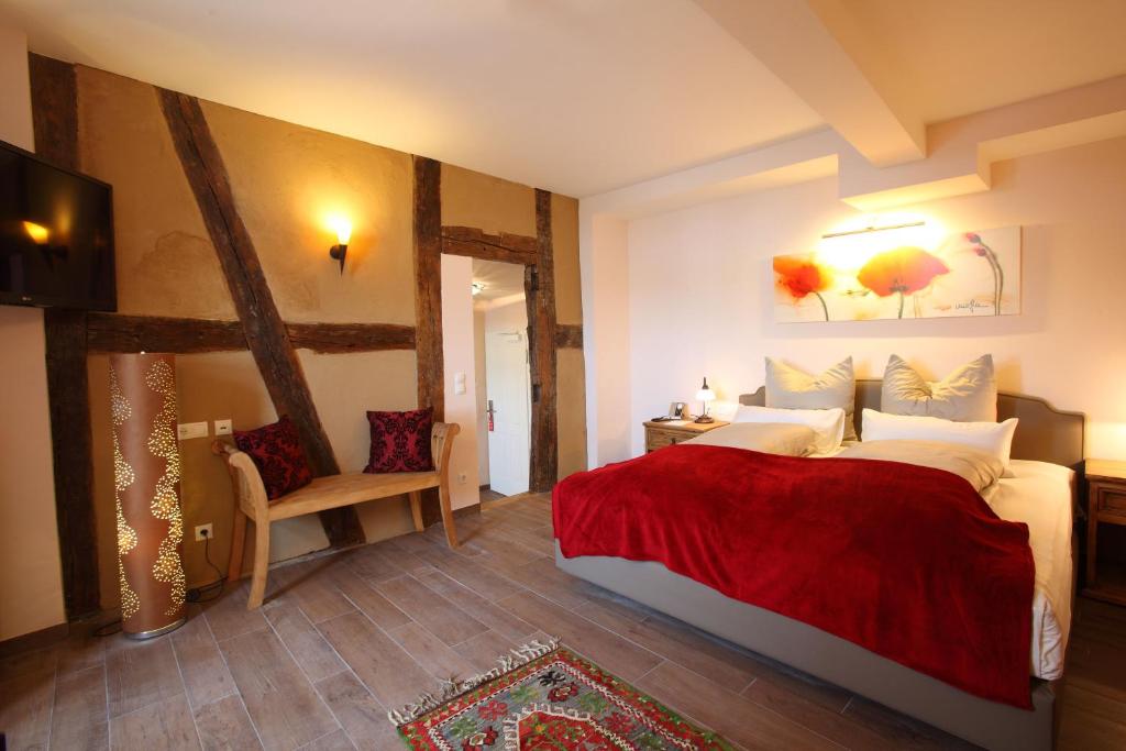 Gemütliches Schlafzimmer mit Holzbalken, Doppelbett mit roter Decke, Holzboden, Sitzbank und Wandbild mit Blumen.